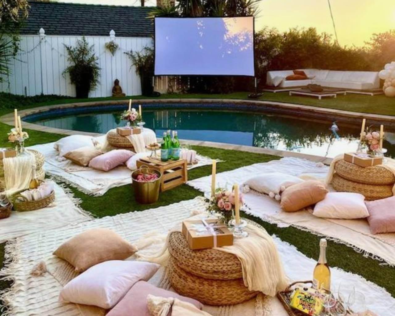 Cozy outdoor movie night for families setup with pillows, blankets, and a projector screen by the pool