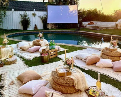 Cozy outdoor movie night for families setup with pillows, blankets, and a projector screen by the pool