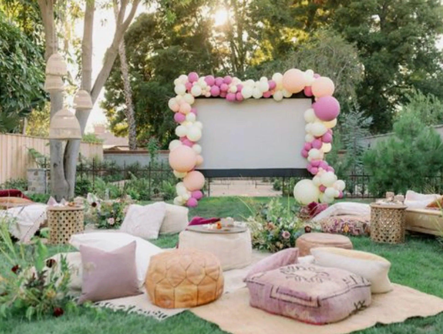 Cozy outdoor movie night for families setup with cushioned seating and balloon-decorated screen in backyard