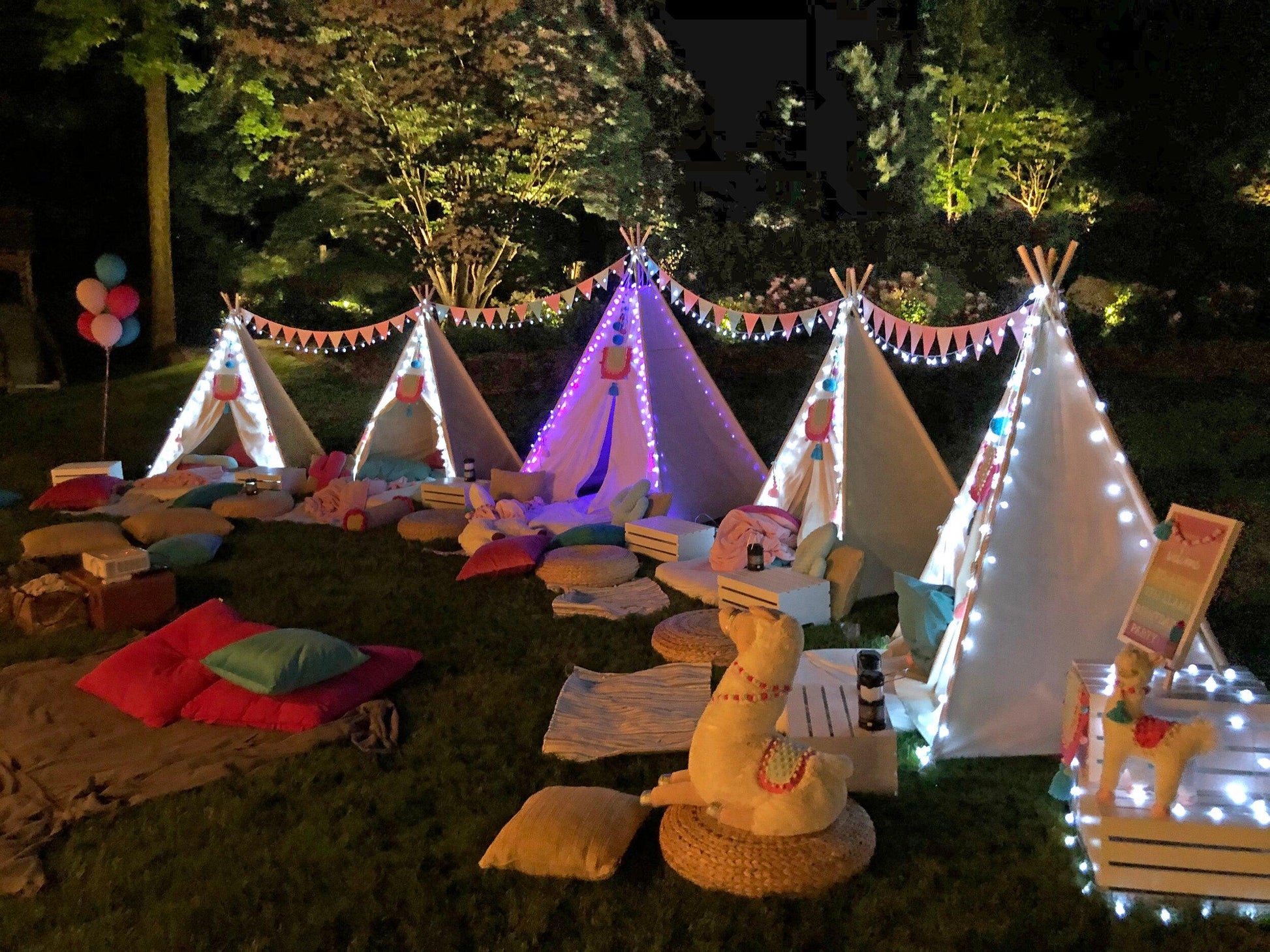 Cozy outdoor movie night for families setup with illuminated tents, cushions, and blankets in a garden