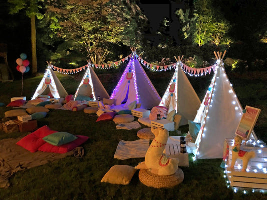 Cozy outdoor movie night for families setup with illuminated tents, cushions, and blankets in a garden